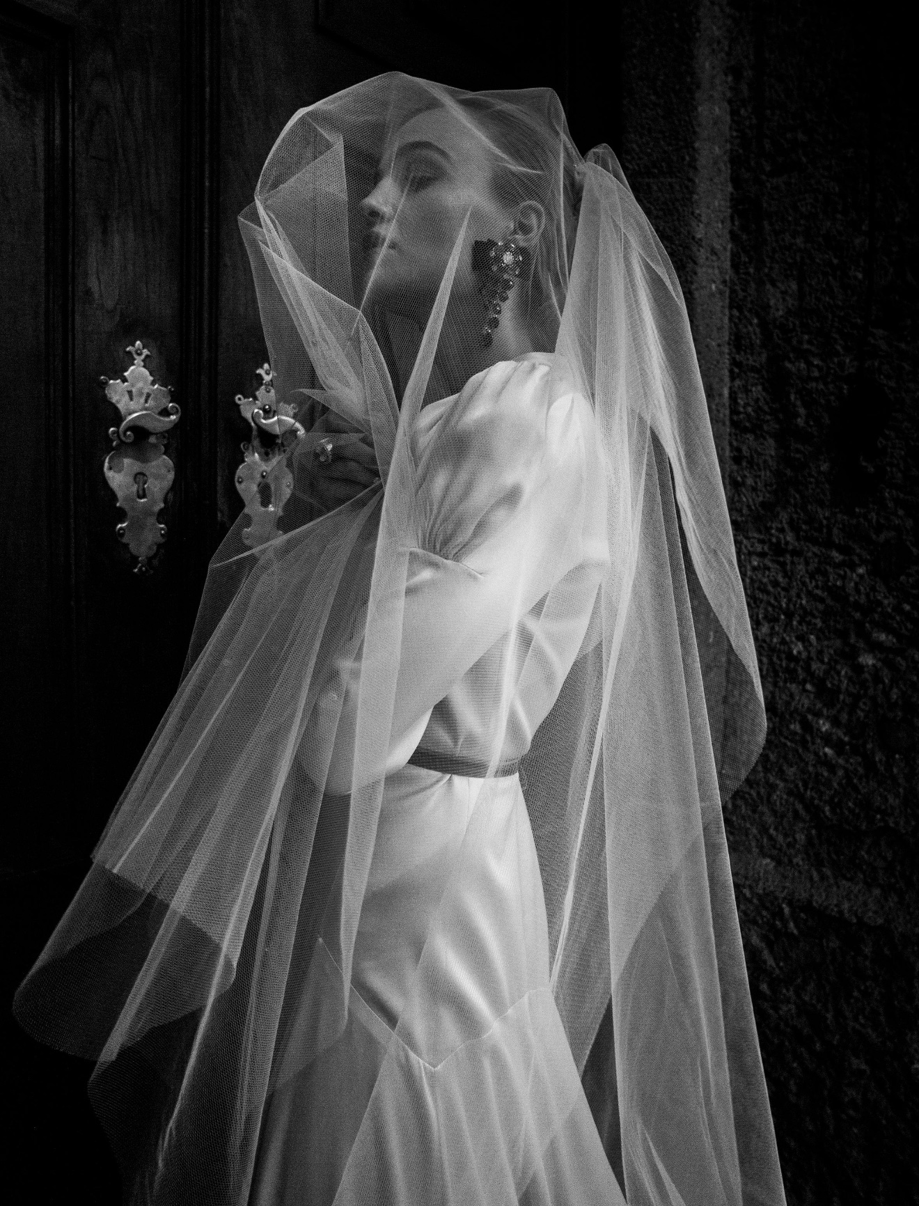 Bride wrapped in a sculptural veil beside an ornate doorway
